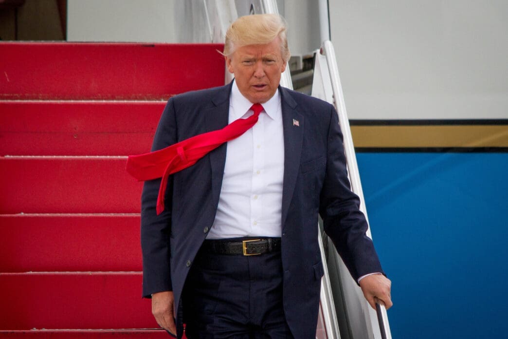 President Trump walks down the red stairs of Air Force One with his red tie blowing sideways.