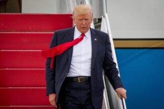 President Trump walks down the red stairs of Air Force One with his red tie blowing sideways.