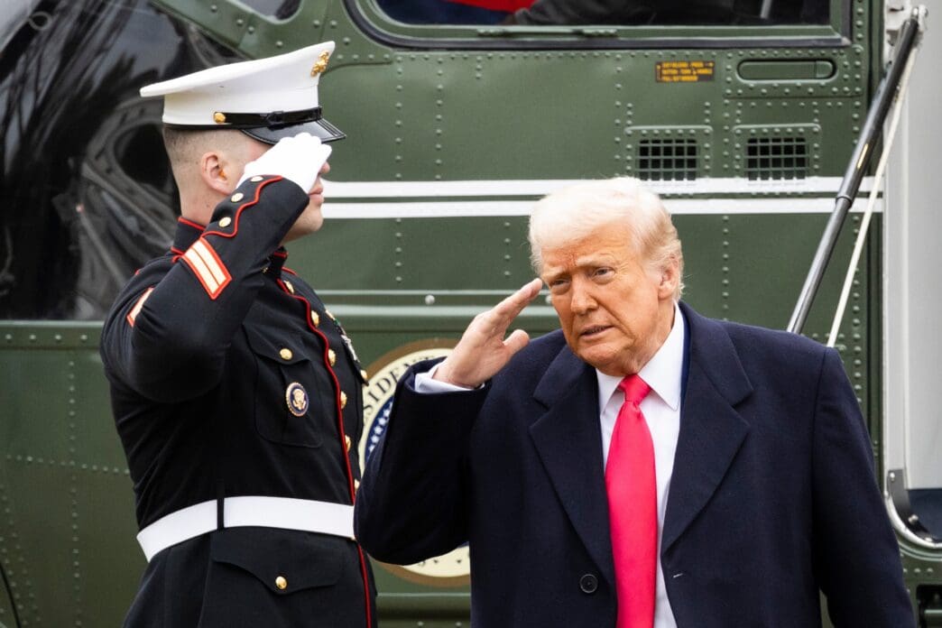 President Trump and a U.S. Marine salute beside Marine One on a cloudy day.