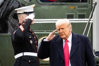 President Trump and a U.S. Marine salute beside Marine One on a cloudy day.