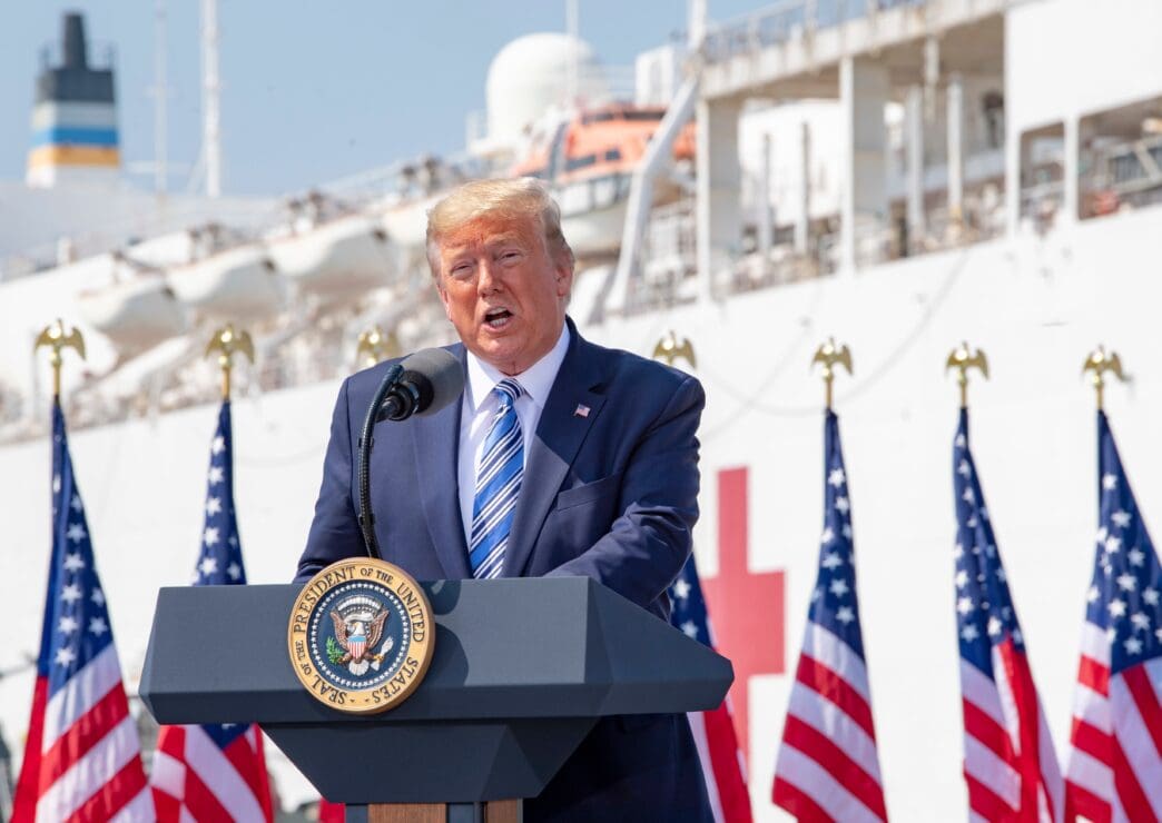 President Trump speaks at a podium in front of the USNS Comfort hospital ship