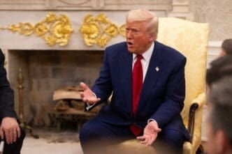 United States President Donald Trump, wearing a blue suit and red tie, sits and gestures while speaking in a yellow armchair inside the White House.