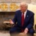 United States President Donald Trump, wearing a blue suit and red tie, sits and gestures while speaking in a yellow armchair inside the White House.