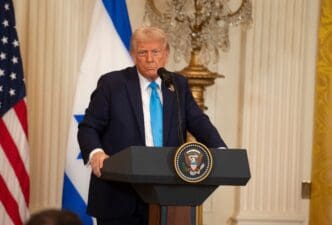 Donald Trump speaks at a podium in the White House with the U.S. and Israel flags behind him.