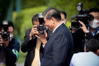 Profile view of President Xi Jinping, surrounded by media photographers and cameramen during an official visit.