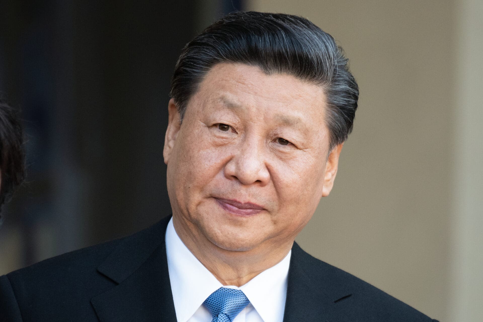 Close-up, head-and-shoulders portrait of Chinese President Xi Jinping wearing a dark suit and blue patterned tie.
