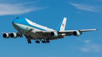 Air Force One, a large blue and white Boeing 747, flies low with its landing gear down.