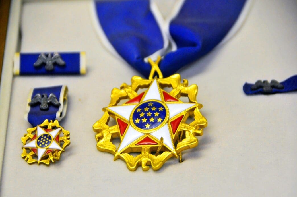 Display case holding the Presidential Medal of Freedom, a gold star with a white and blue center, shown with its ribbon and miniature versions.