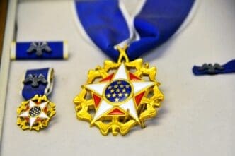 Display case holding the Presidential Medal of Freedom, a gold star with a white and blue center, shown with its ribbon and miniature versions.