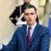 Spanish Prime Minister Pedro Sánchez gestures while speaking outdoors at the Élysée Palace, with military guards in the blurred background.