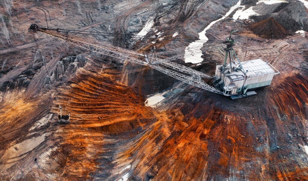 High-angle drone view of a massive walking excavator digging in an open-pit mine of striated red, orange, and brown earth