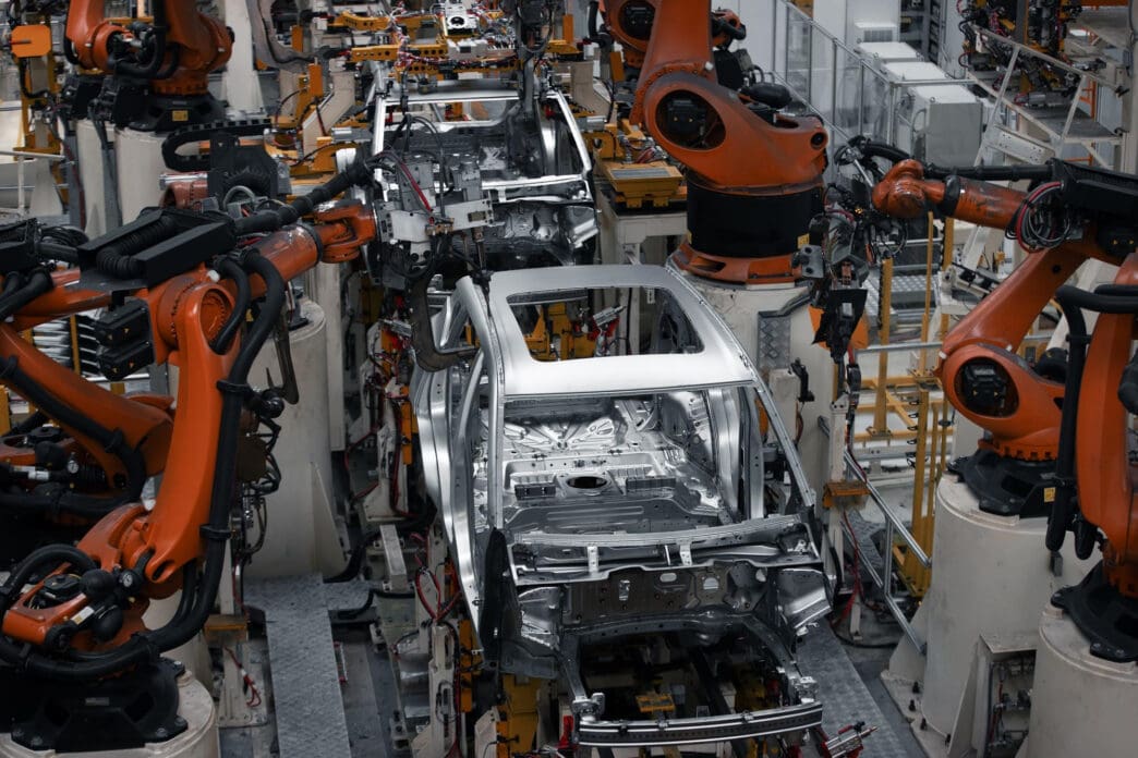 Top view of robotic arms welding a car frame on an automotive assembly line.