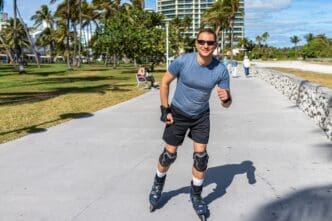 Fit man roller skating on a sunny boardwalk in Lummus Park, South Beach, wearing protective gear.