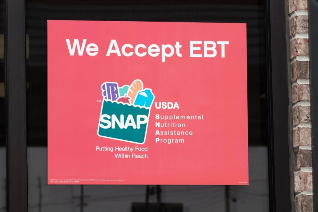A red sign posted in a store window reading "We Accept EBT" and displaying the USDA SNAP logo.