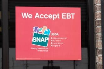 A red sign posted in a store window reading "We Accept EBT" and displaying the USDA SNAP logo.
