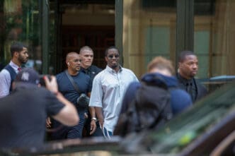 Sean Combs exits a hotel flanked by security with paparazzi nearby