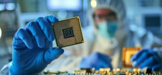 Gloved hands of a technician in a cleanroom suit holding up a central processing unit (CPU) chip for inspection.