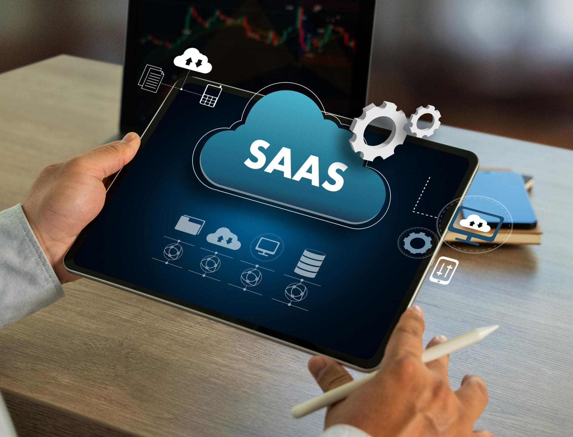 Hands holding a tablet displaying a large cloud icon with "SaaS" in white letters, surrounded by gears and technology icons