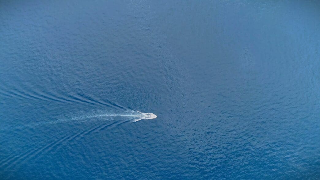 A white speedboat cuts through blue ocean water, leaving a foamy wake behind it.