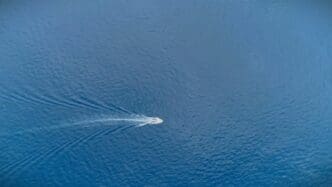 A white speedboat cuts through blue ocean water, leaving a foamy wake behind it.