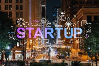 The word "STARTUP" glowing in neon over a long city street at night, surrounded by business and technology icons.