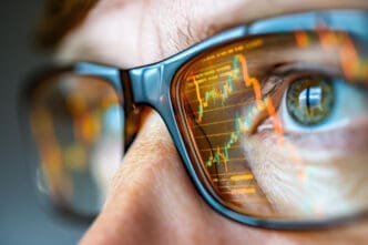 Close-up of eyeglasses reflecting a bright orange stock market chart showing volatility.