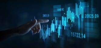 A person's hand pointing at a glowing blue stock market graph on a digital touchscreen.