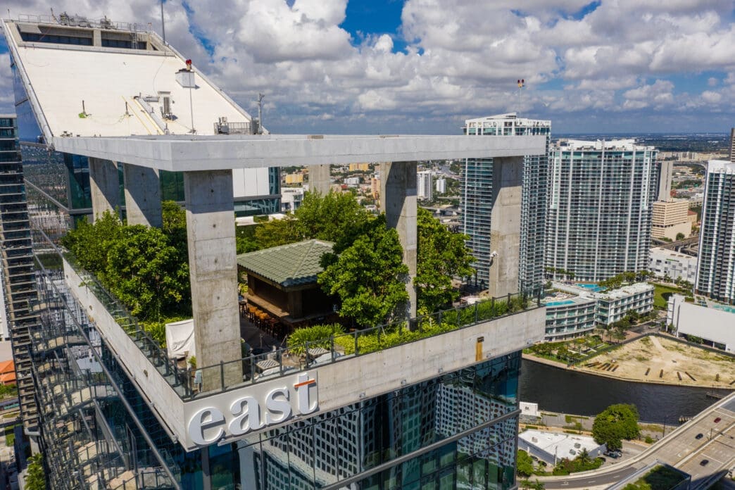 An aerial view of the Sugar rooftop bar at the EAST Miami hotel, showing its lush garden setting above the Brickell skyline.