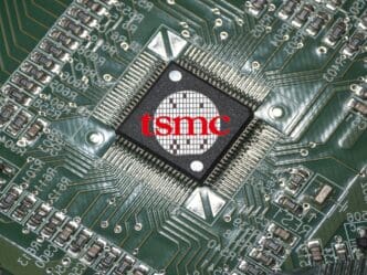 A close-up of a "tsmc" logo on a microchip set on a green circuit board.