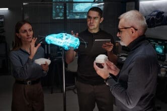 Three automotive engineers review a glowing blue holographic projection of a sports car while holding physical 3D-printed prototypes