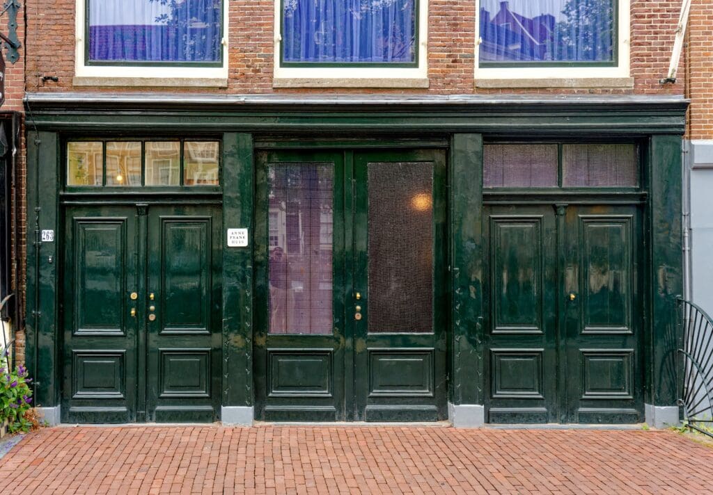 The dark green doors at the entrance to the historic Anne Frank House museum on a brick street in Amsterdam.