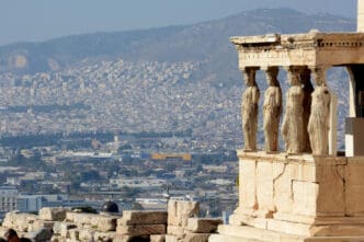 The ancient Porch of the Caryatids on the Acropolis overlooks the vast, modern cityscape of Athens, Greece.