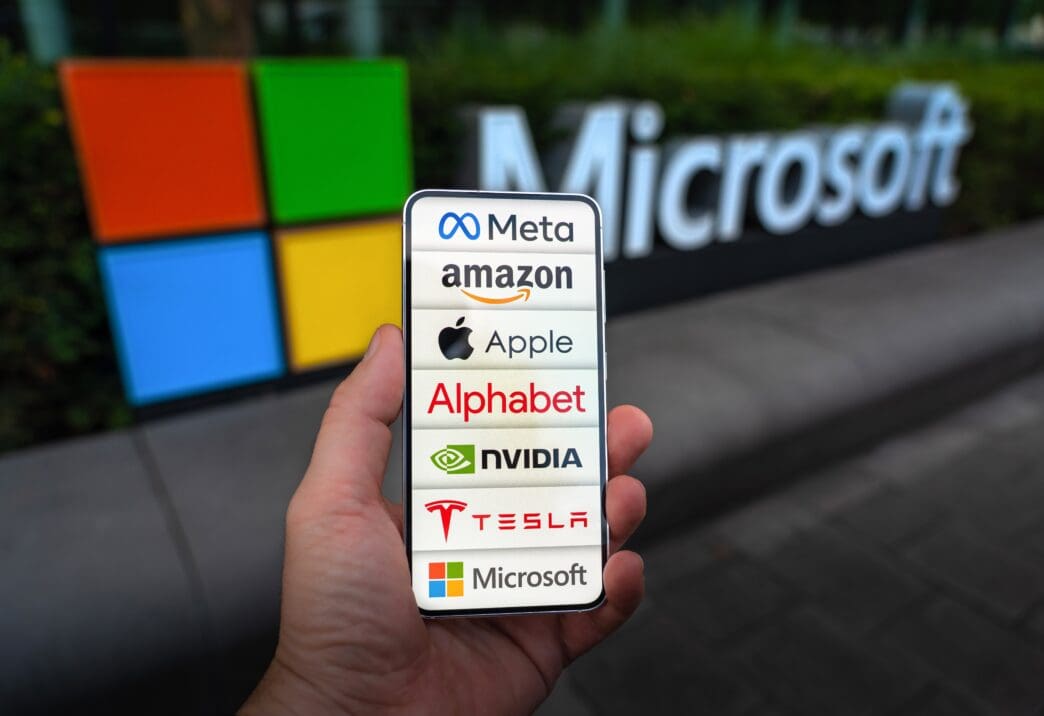 A hand holding a smartphone displaying the logos of the Magnificent Seven tech companies