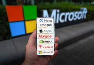 A hand holding a smartphone displaying the logos of the Magnificent Seven tech companies