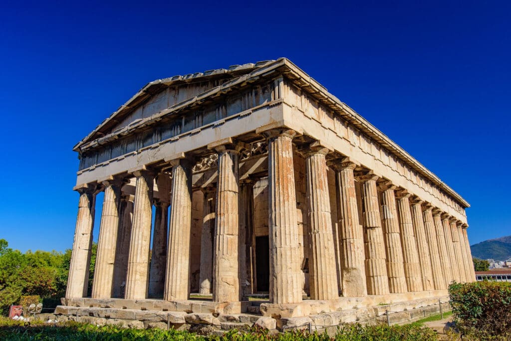 The remarkably well-preserved Temple of Hephaestus in Athens, with its Doric columns, stands fully intact against a vibrant blue sky.