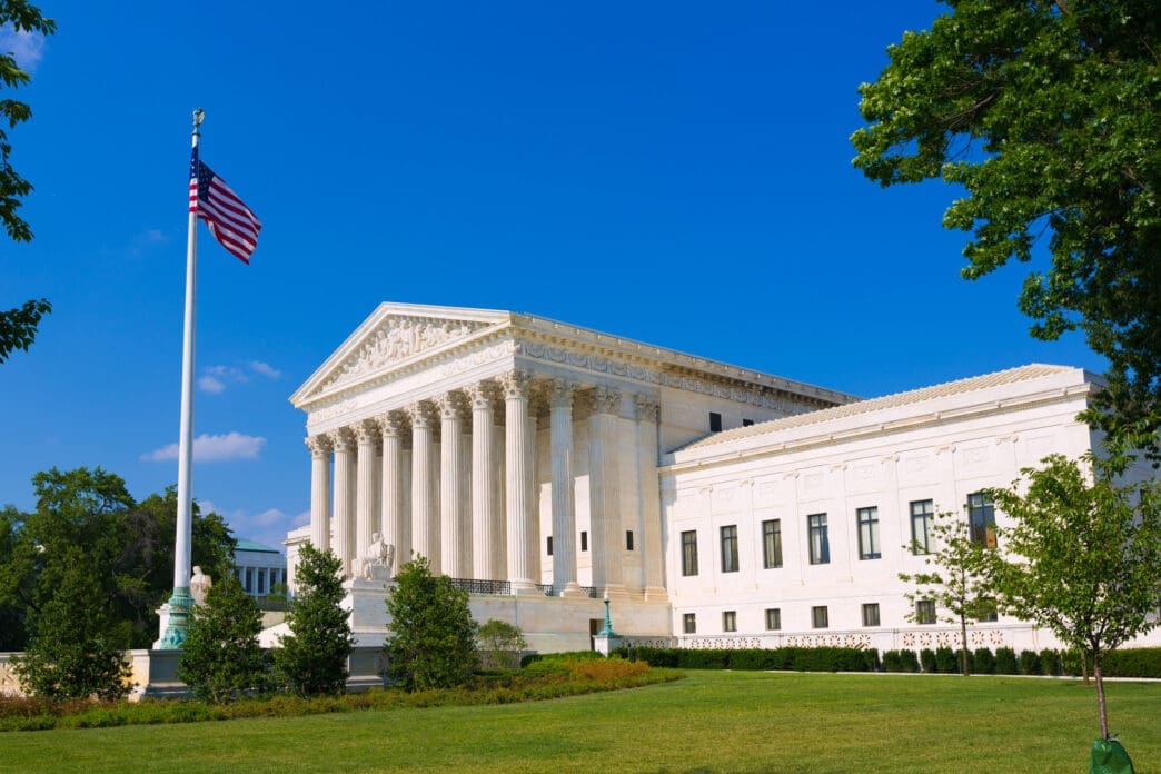 The US Supreme Court building and its lawn on a sunny day, framed by green trees.