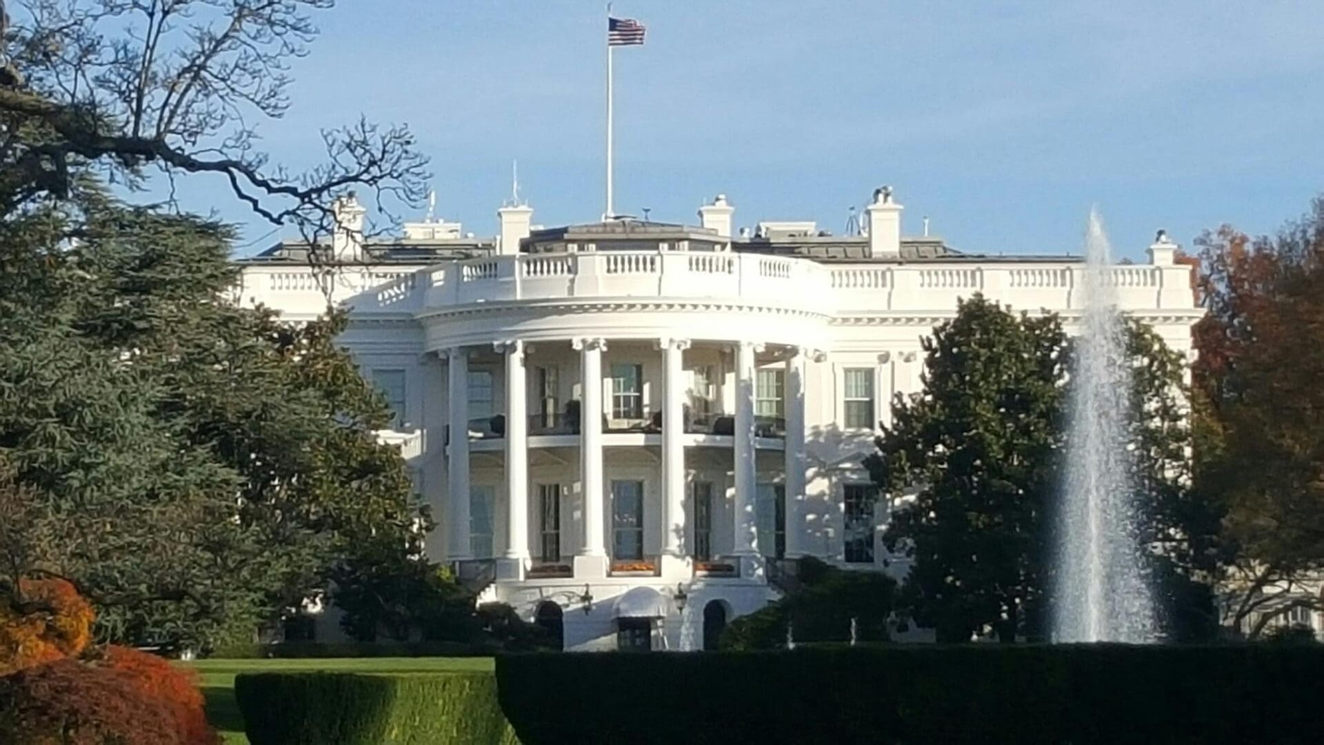 The White House with an American flag flying and a fountain in the foreground