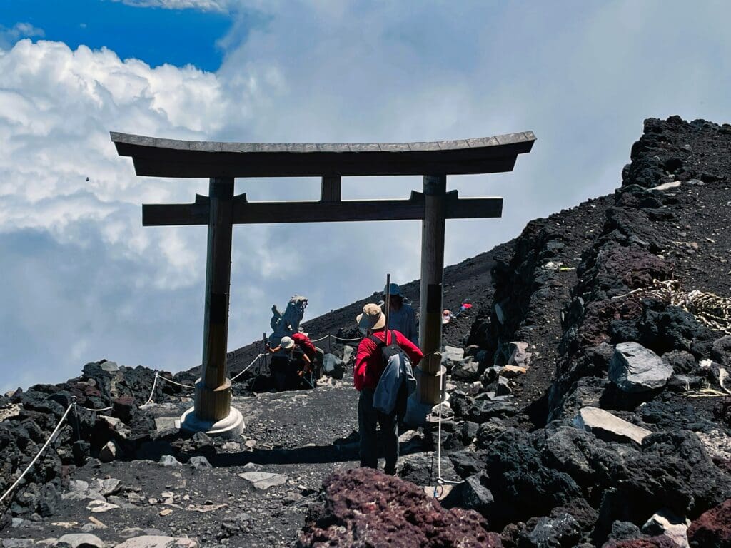 Hikers walk through a torii gate on the rocky Gotemba Trail near the summit of Mount Fuji, Japan.