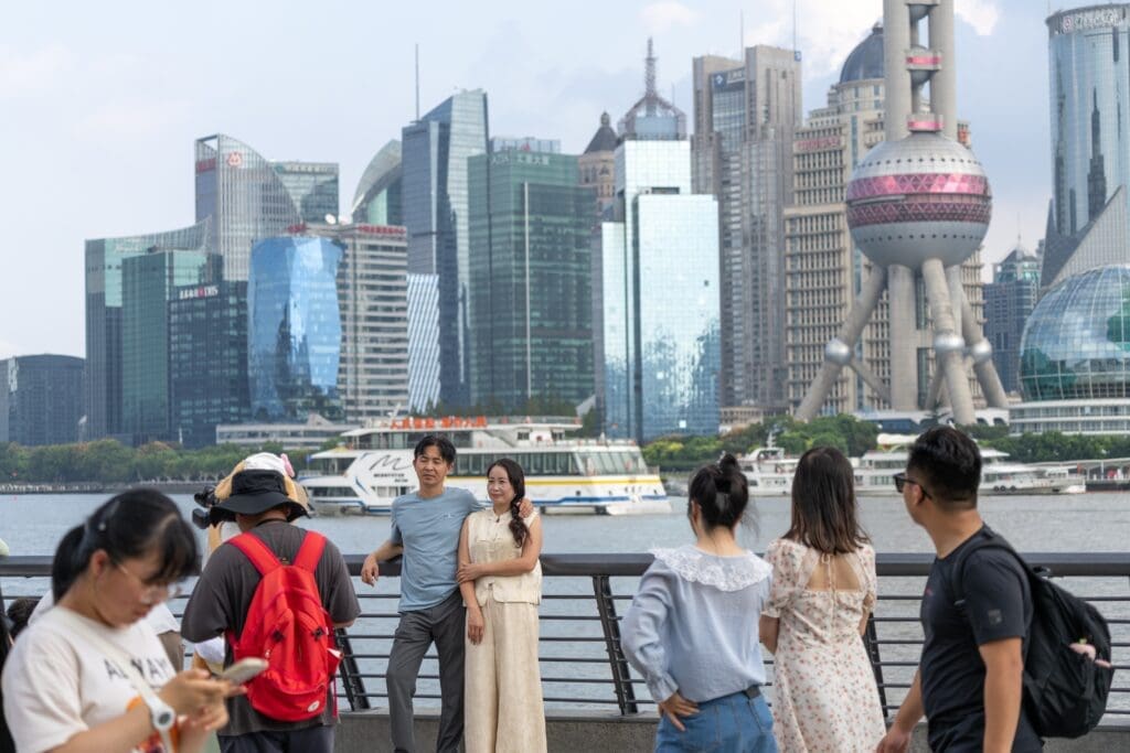 Tourists posing for a photo on the Bund waterfront promenade with the futuristic Pudong skyline and Oriental Pearl Tower behind them