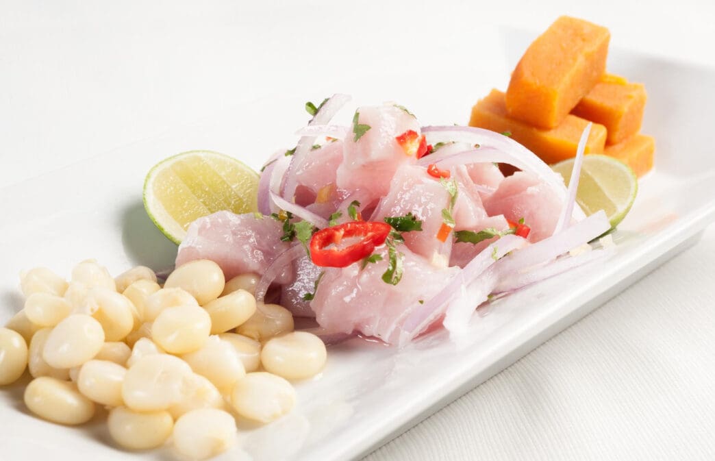 A serving of Peruvian ceviche with diced white fish, red onion, chili slices, and lime, accompanied by parboiled corn and sweet potato.