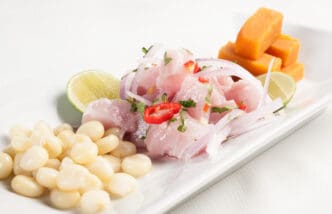 A serving of Peruvian ceviche with diced white fish, red onion, chili slices, and lime, accompanied by parboiled corn and sweet potato.