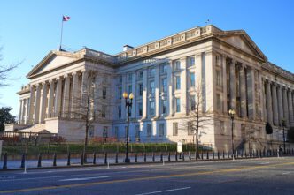 The massive, columned facade of the historic U.S. Department of the Treasury building in Washington, D.C., under a clear blue sky.
