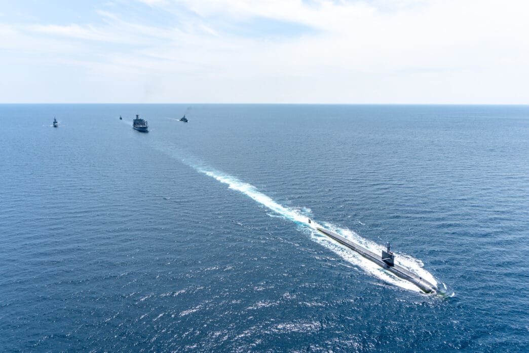 The U.S. Navy submarine USS Louisville (SSN-724) sails on the ocean's surface, leading a fleet of ships during an exercise.