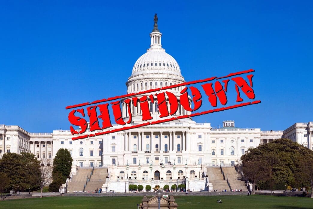 The US Capitol building under a clear blue sky with a red "SHUTDOWN" stamp