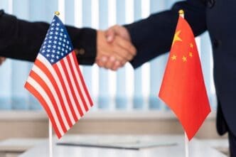 US and China flags in front of diplomats shaking hands during negotiations.