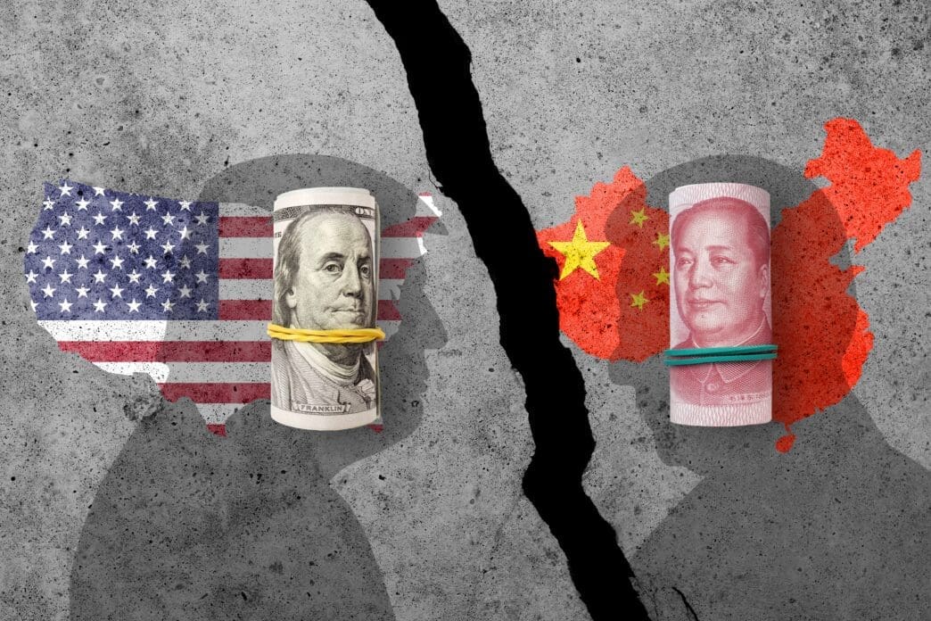 A cracked concrete wall separates rolled US dollar bills and a US map flag from rolled Chinese yuan bills and a China map flag, symbolizing trade conflict.