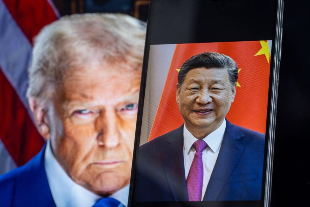 Smartphone shows Xi Jinping's portrait in front of a computer screen showing Donald Trump.