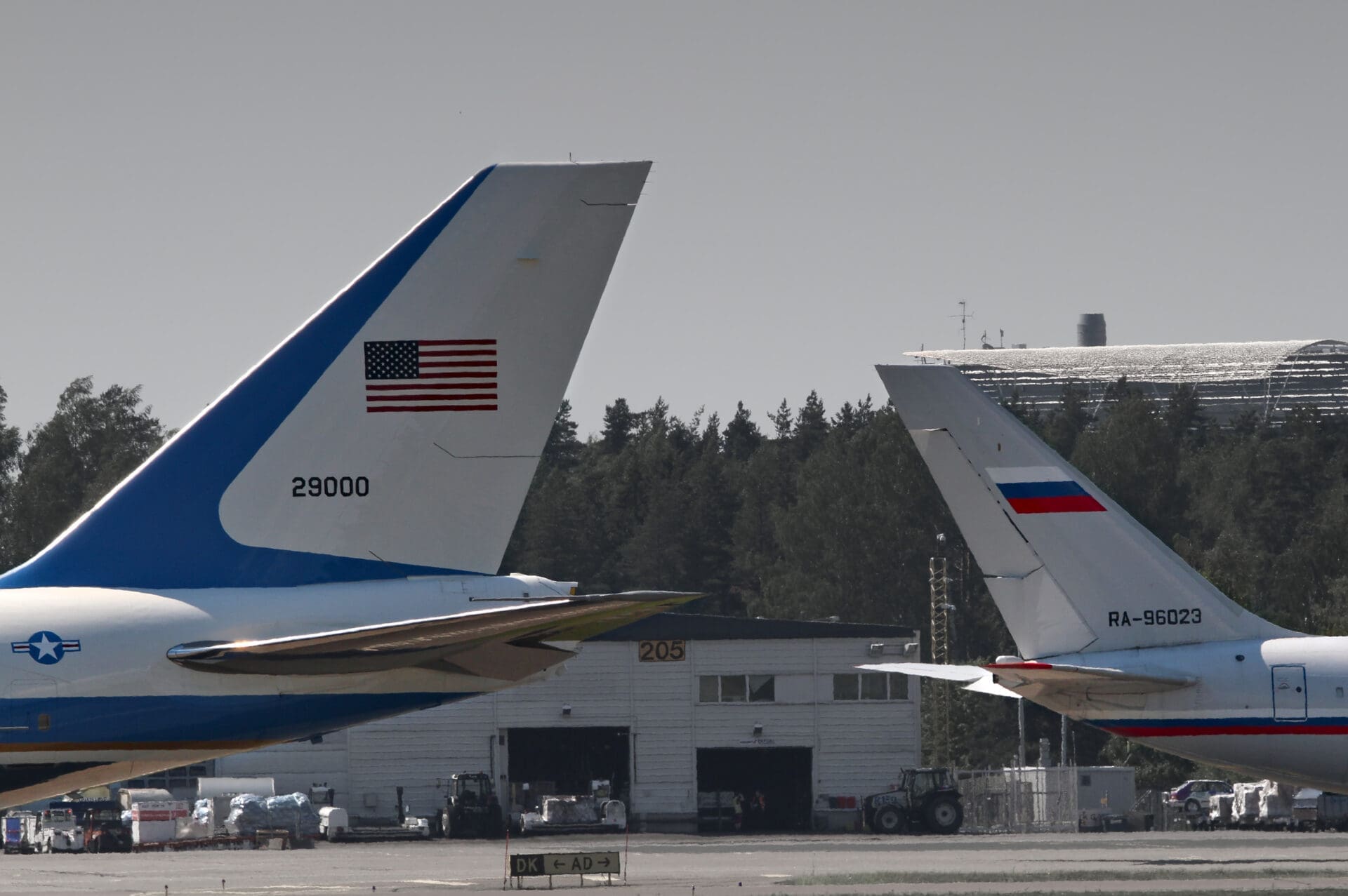 The tail fins of the US Air Force One (Boeing 747) and a Russian government Ilyushin Il-96 aircraft are parked close together on an airport tarmac.