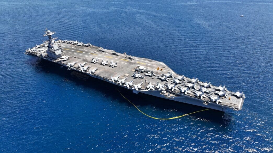 Aerial drone photo of the USS Gerald R. Ford aircraft carrier at sea with planes on deck.