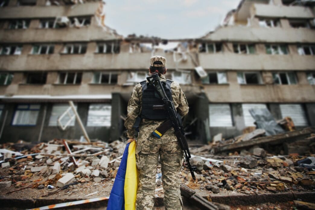 Ukrainian soldier holds the Ukrainian flag in front of a destroyed building